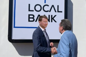 two business men shaking hands in front of a business sign